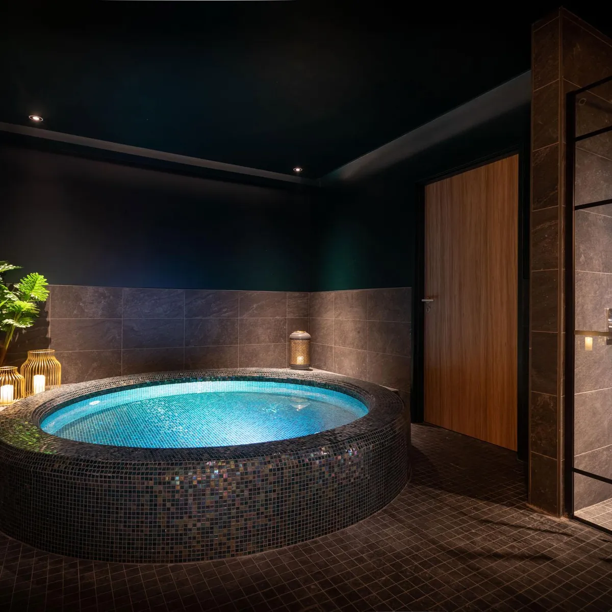Salle de bain luxueuse avec un grand bain circulaire entouré de mosaïques, des bougies allumées sur une table et une plante verte