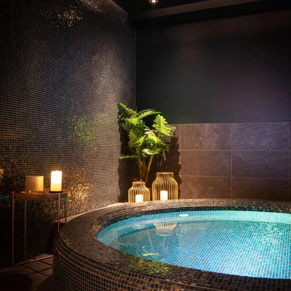 Piscine intérieure avec éclairage bleu, entourée de mosaïques colorées, et décorée de plantes et de lanternes