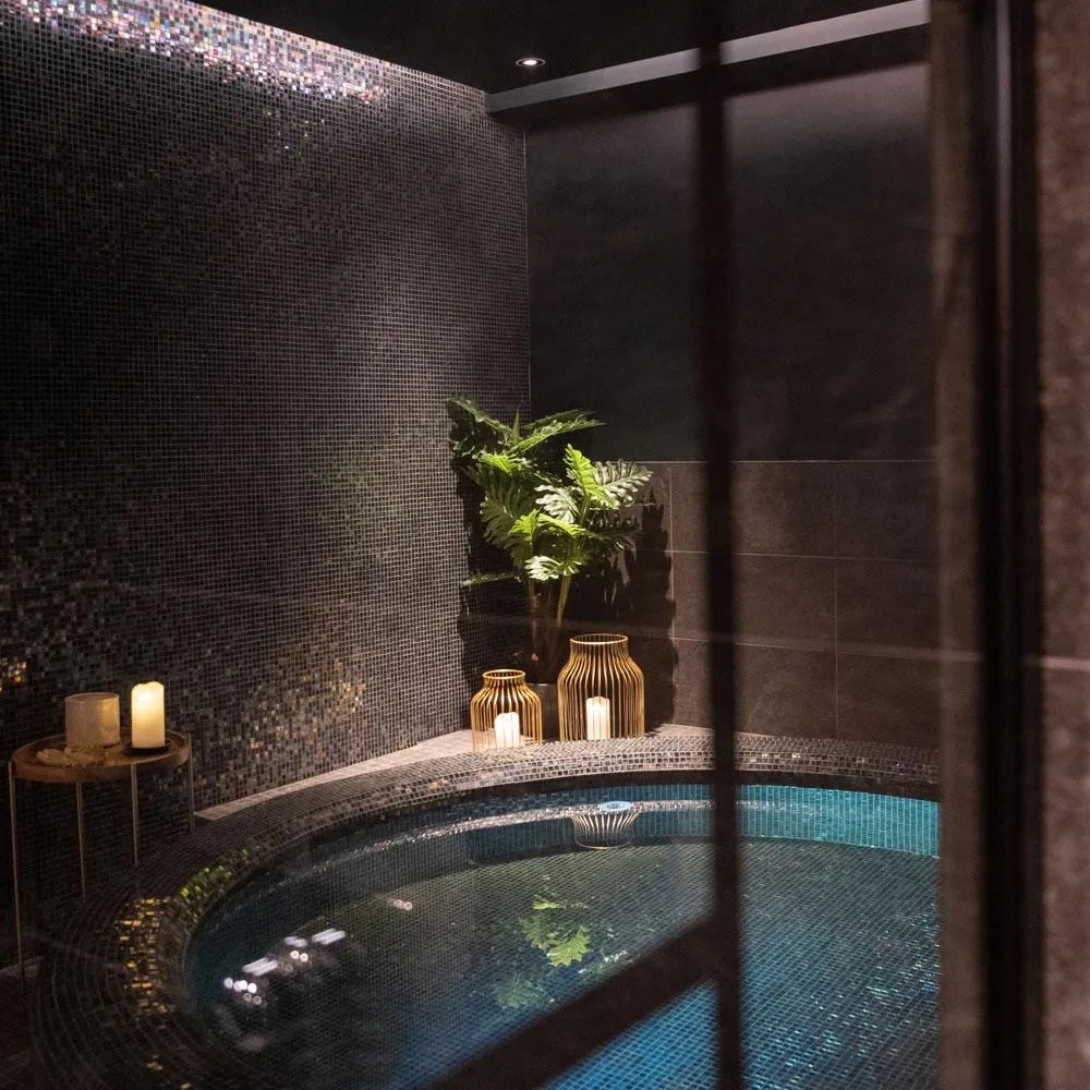 Piscine intérieure avec mosaïque bleue, plantes et bougies sur une étagère murale