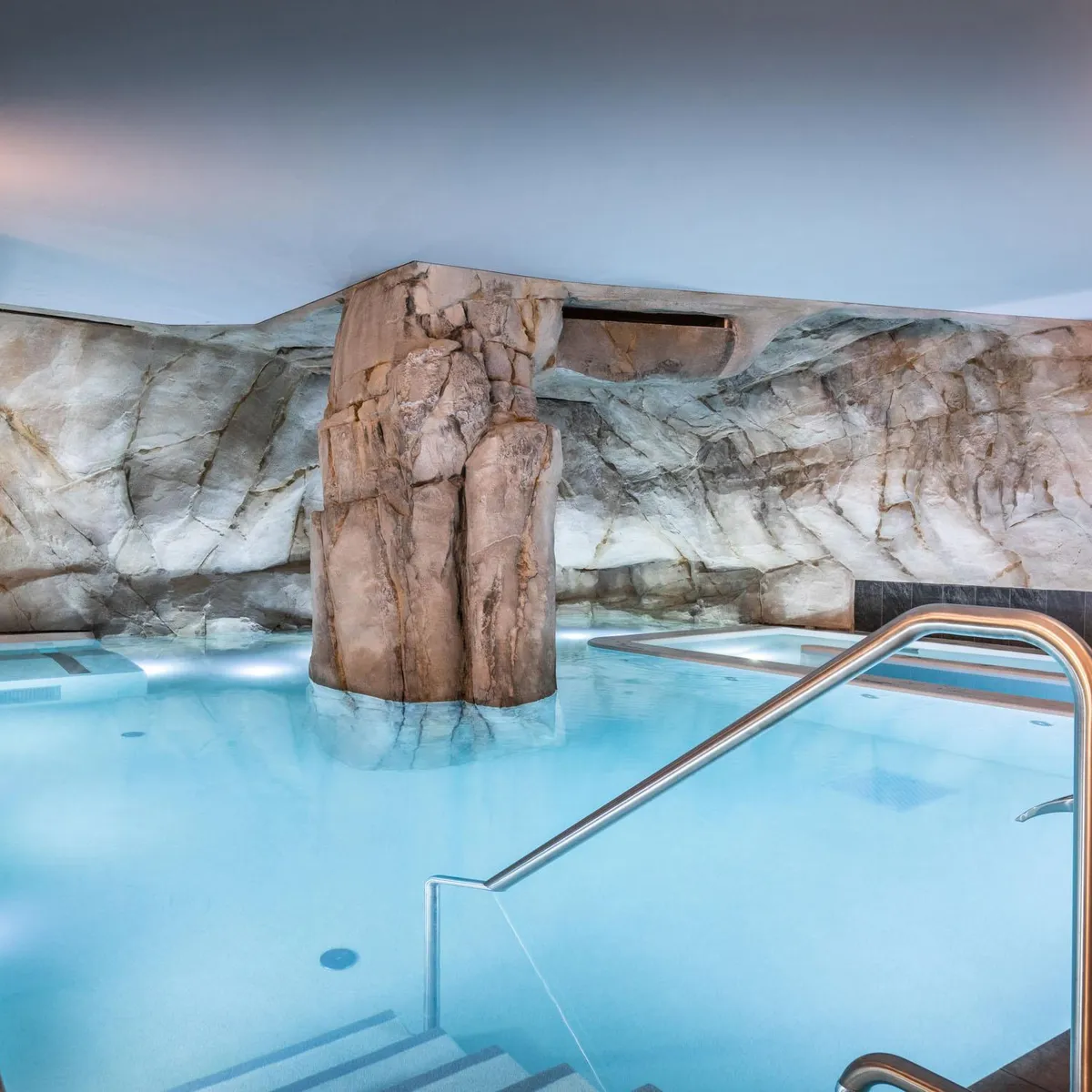 Piscine intérieure avec une grande paroi rocheuse et des marches métalliques pour l'accès