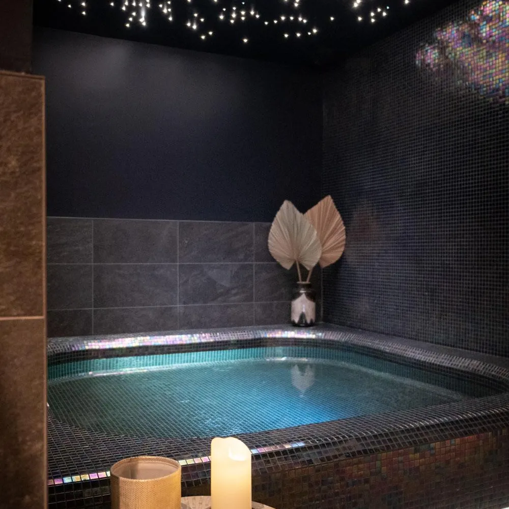 Piscine intérieure éclairée avec une bougie allumée et un vase sur une table à proximité