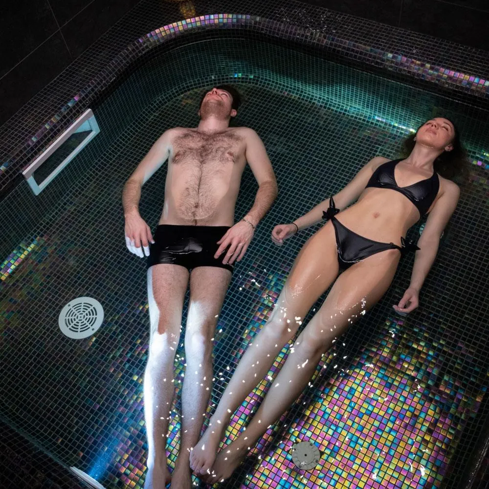 Deux personnes allongées dans un bain à remous avec des jets d'eau, l'homme torse nu et la femme en maillot de bain noir