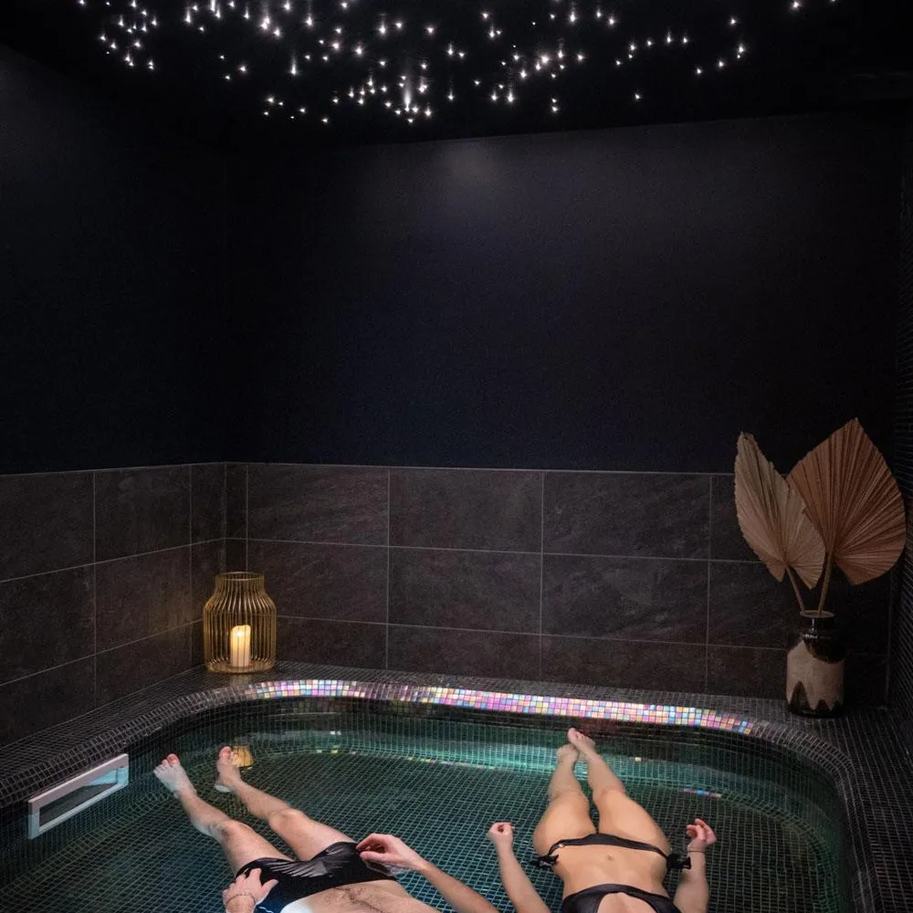 Deux personnes allongées dans un bain à remous avec des lumières sous-marines colorées, sous un plafond décoré de guirlandes lumineuses