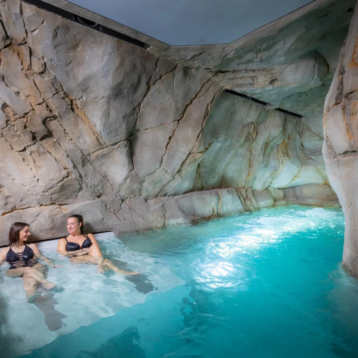 Deux personnes sont assises dans un bassin d'eau turquoise entouré de parois rocheuses