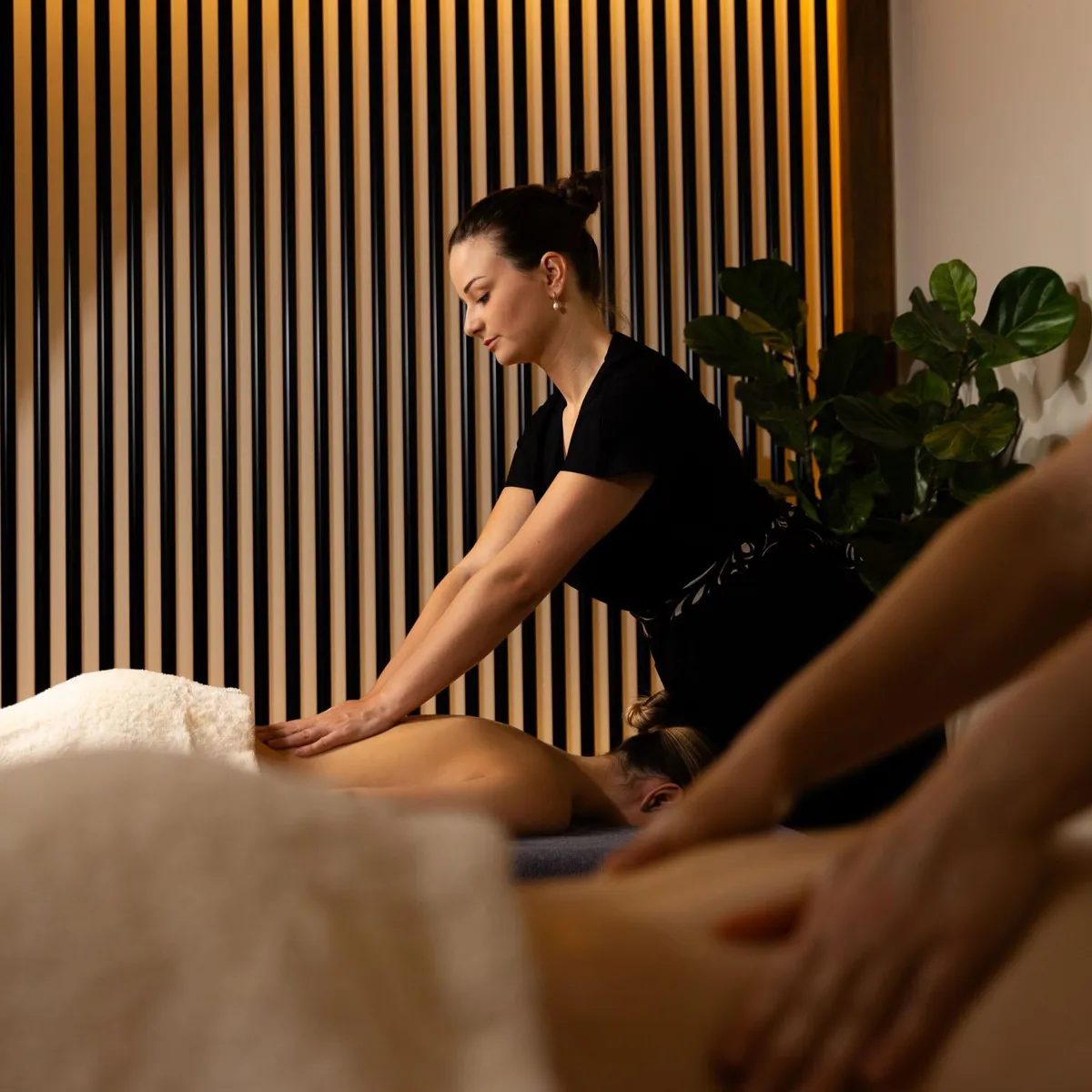 Une personne en tenue noire donne un massage à une personne allongée sur le ventre sur une table recouverte d'une serviette