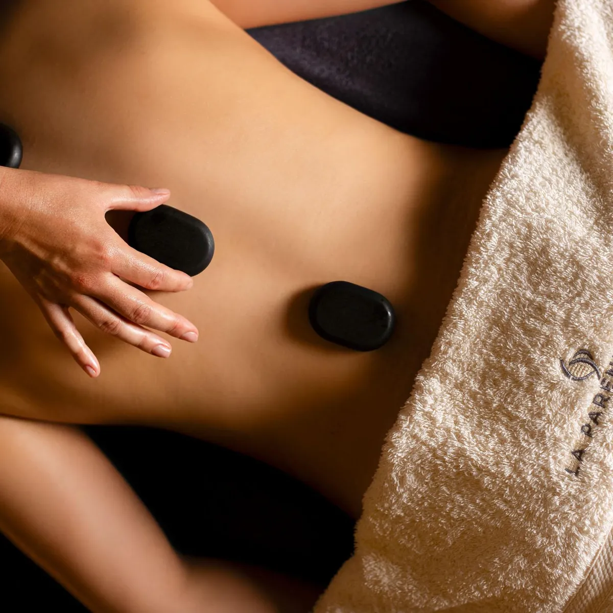 Une personne reçoit un massage aux pierres chaudes sur le dos, recouvert partiellement d'une serviette