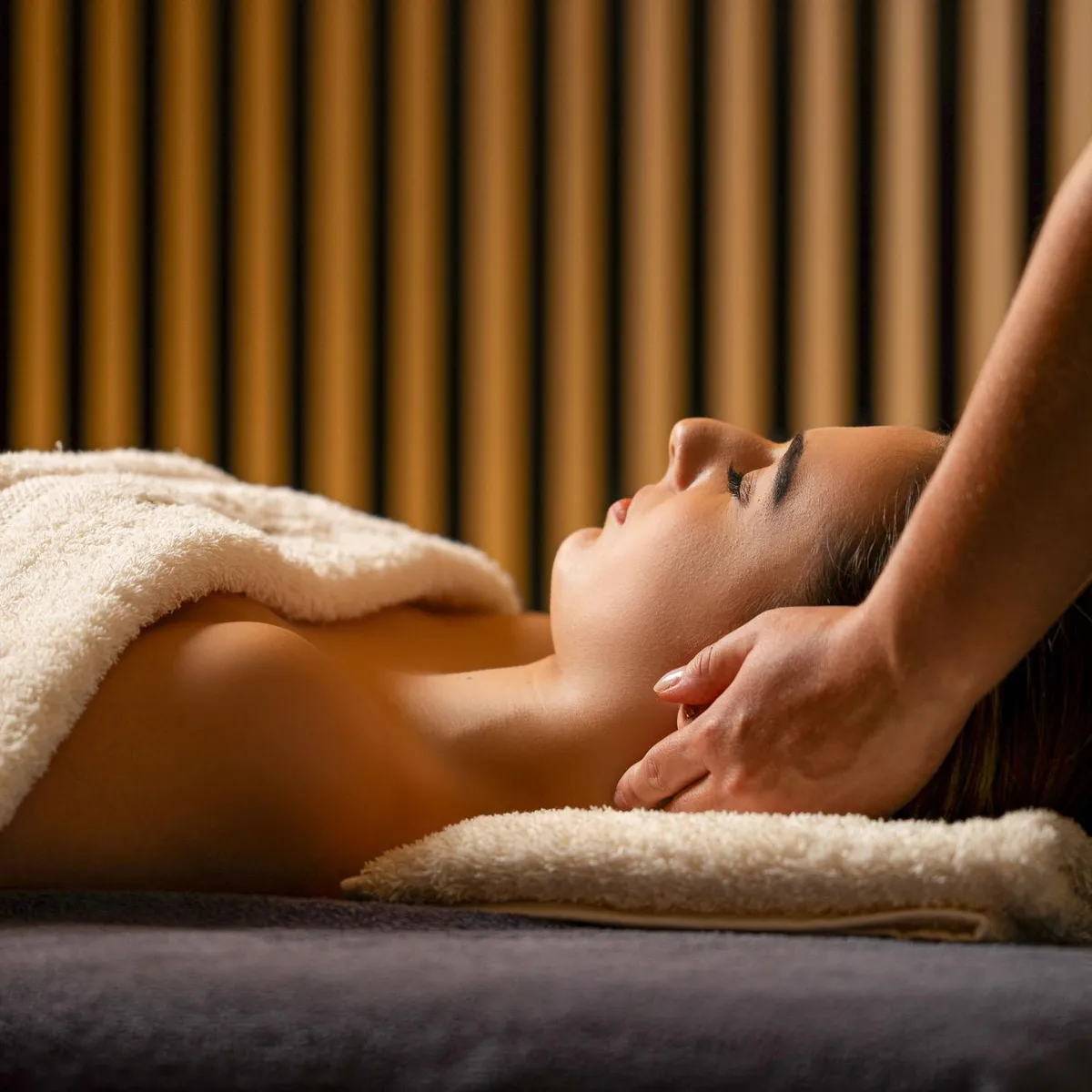 Une personne reçoit un massage sur un lit de massage recouvert de serviettes, dans une pièce aux murs à rayures verticales