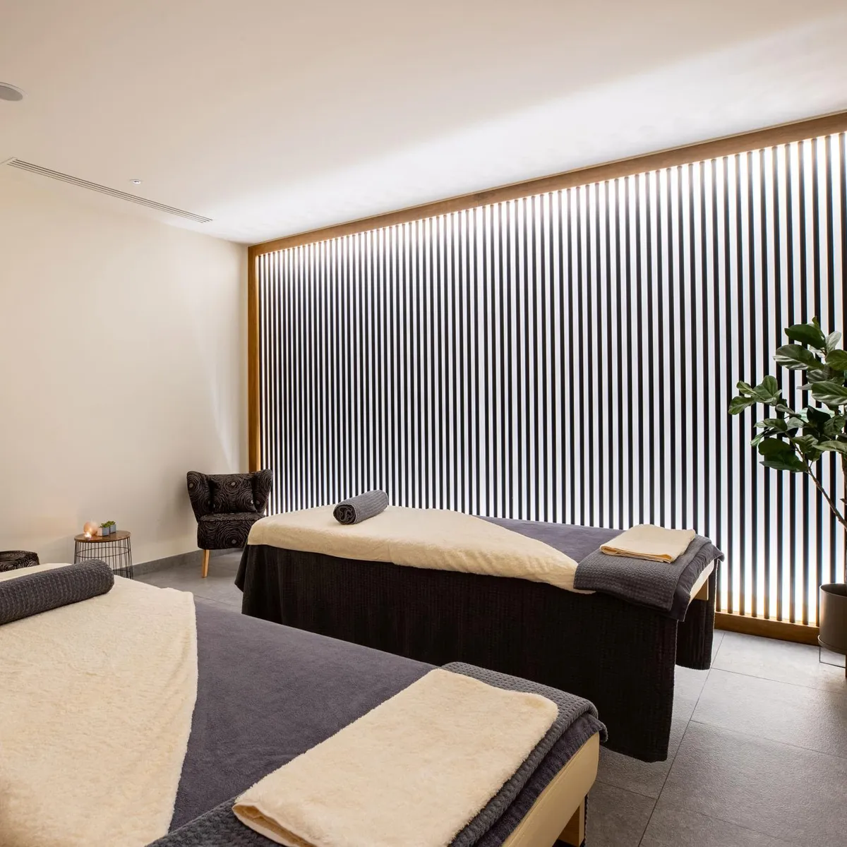 Salle de massage avec deux tables de massage, des serviettes, une plante et des chandelles
