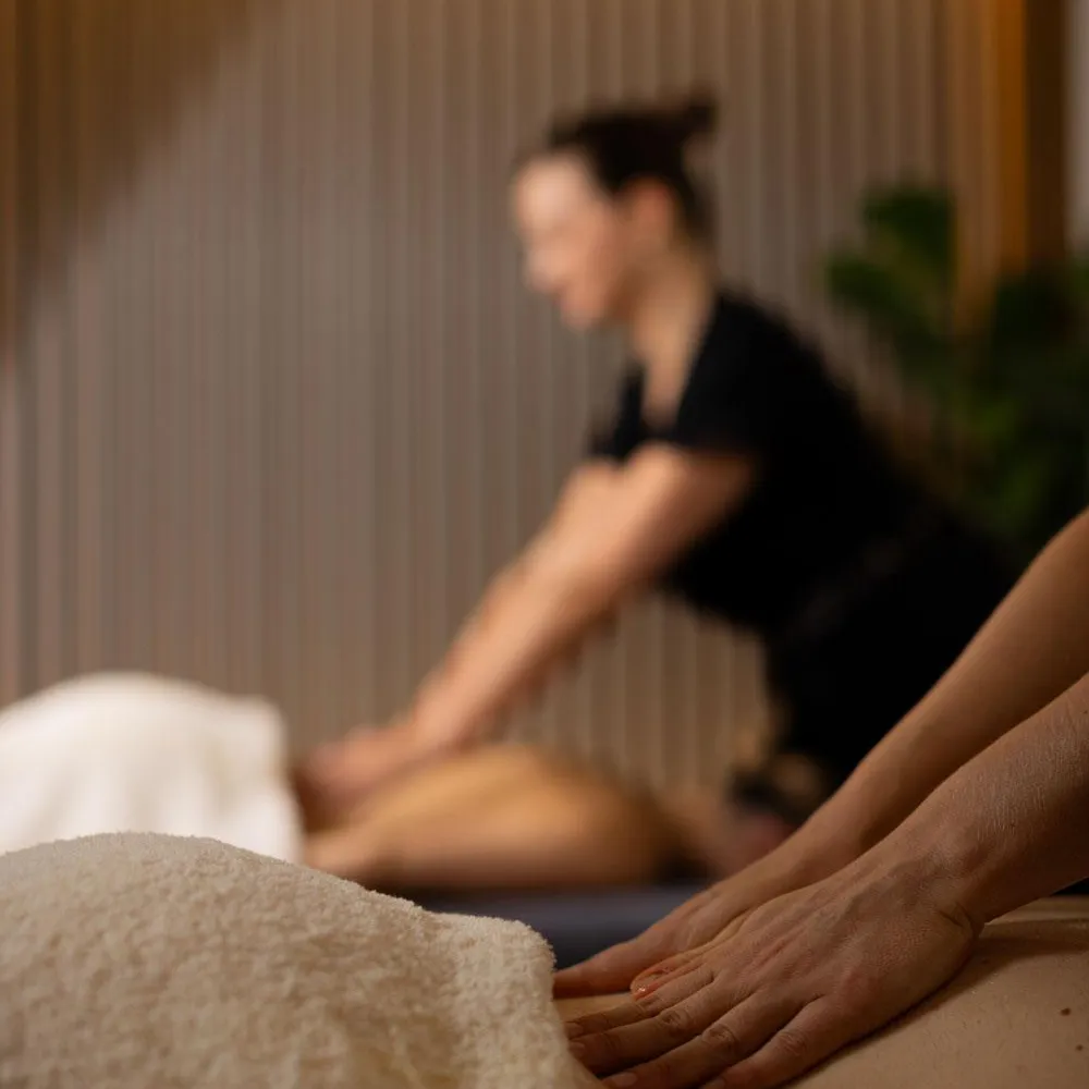 Une personne reçoit un massage sur une table recouverte d'une serviette, avec une autre personne en arrière-plan flou