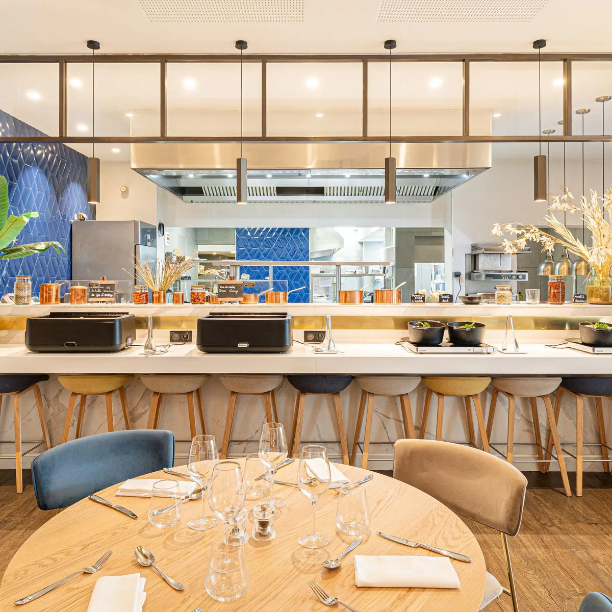 Un restaurant avec une cuisine ouverte, des tabourets de bar et une table dressée avec des verres et des couverts