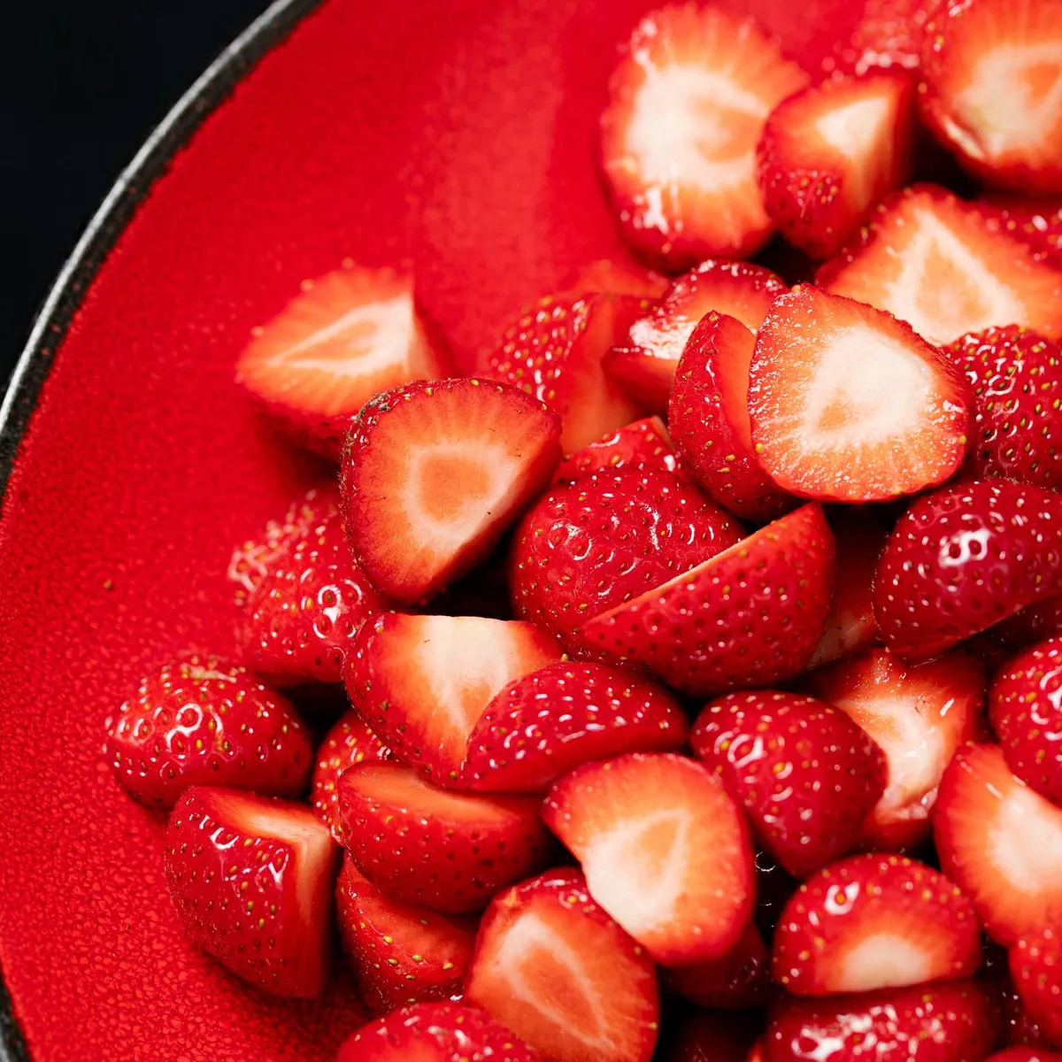 Des morceaux de fraises coupées en deux dans un plat rouge