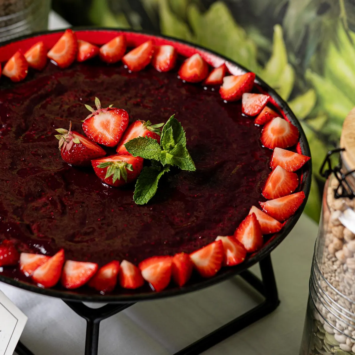 Mousse au chocolat garnie de fraises et de feuilles de menthe, présentée sur un plateau avec une étiquette et entourée de bocaux de légumineuses