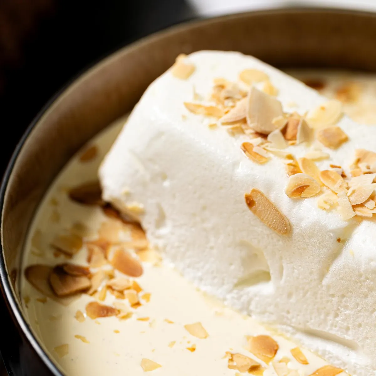 Une part de dessert blanc garnie de copeaux d'amandes dans un plat noir