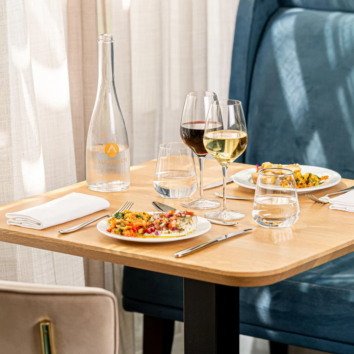 Table dressée avec deux assiettes de nourriture, deux verres de vin, une bouteille d'eau et des verres d'eau, avec des serviettes et des couverts