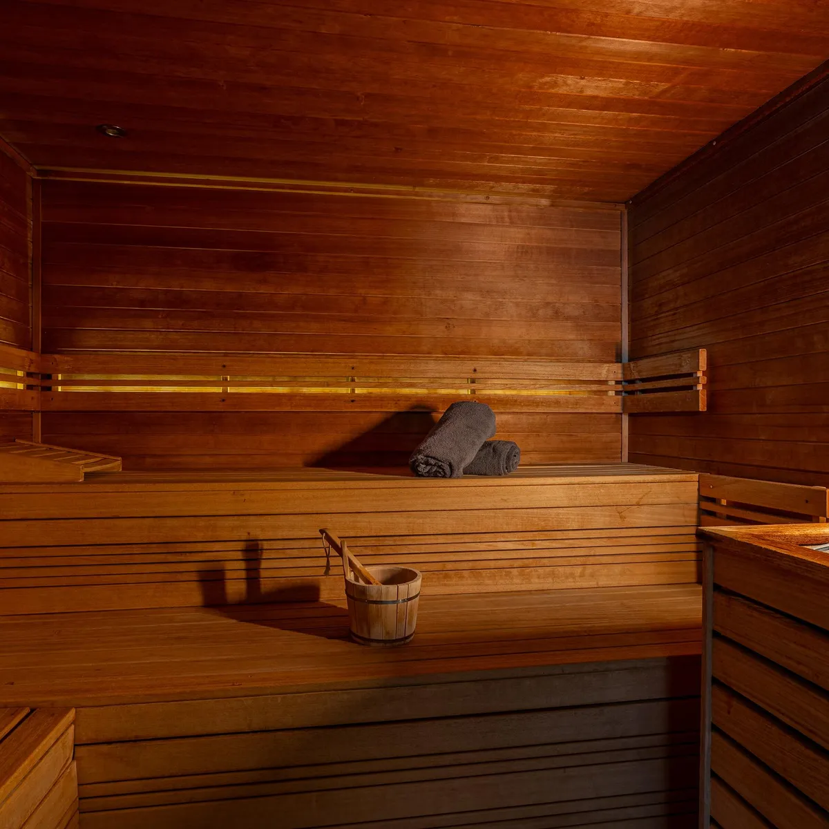 Intérieur d'un sauna en bois avec des bancs, un seau en bois et des pierres chaudes