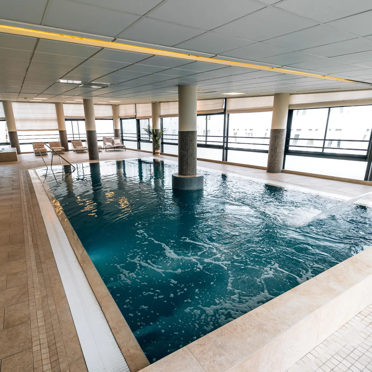 Piscine intérieure avec des colonnes et des chaises longues devant de grandes baies vitrées