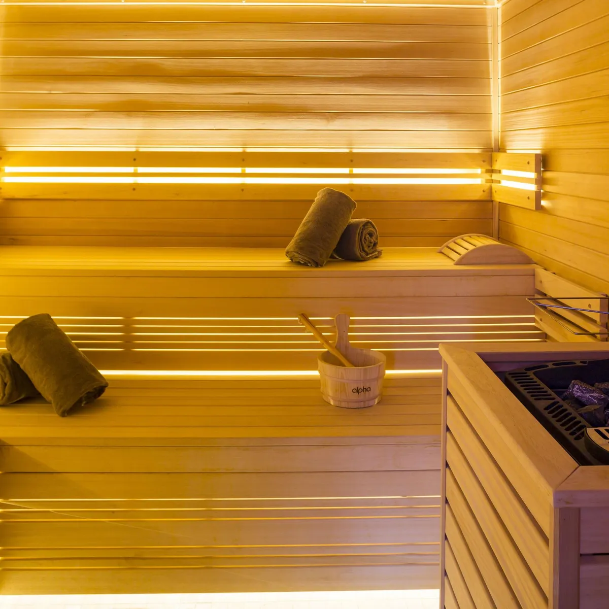 Salle de sauna en bois avec bancs, seau et louche en bois, et pierres chauffées sur un poêle