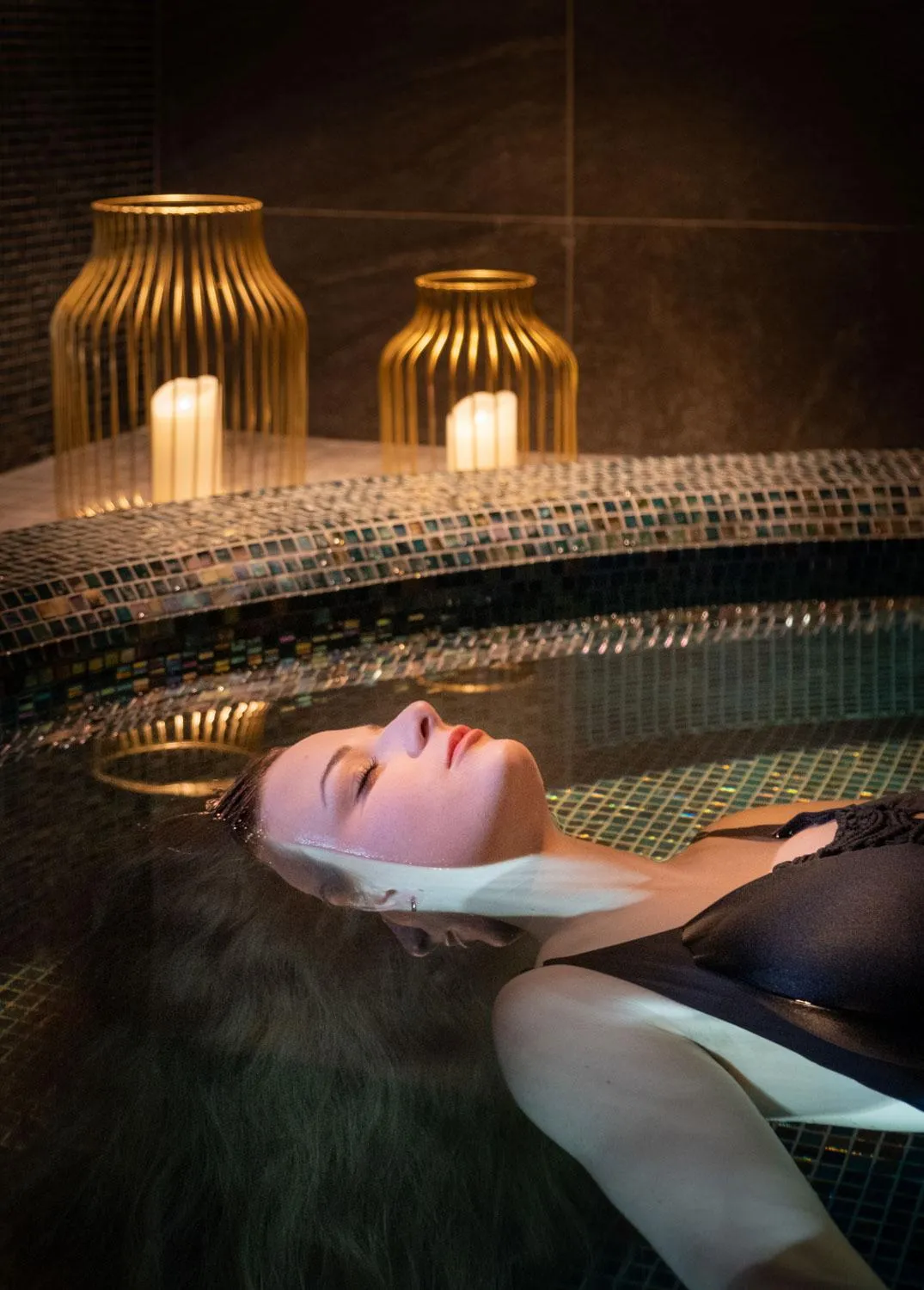 Une personne allongée dans un bain à remous avec des bougies allumées en arrière-plan