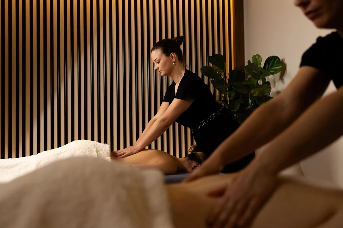Une personne en tenue noire donne un massage à une personne allongée sur le ventre sur une table recouverte d'une serviette