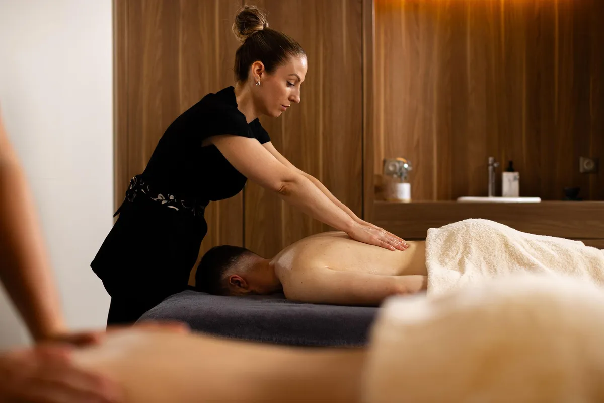 Une femme en tenue noire donne un massage à une personne allongée sur le ventre sur une table de massage recouverte d'une serviette