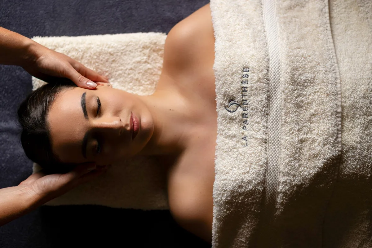 Une personne allongée sur le ventre reçoit un massage sur la tête, couverte d'un drap de massage
