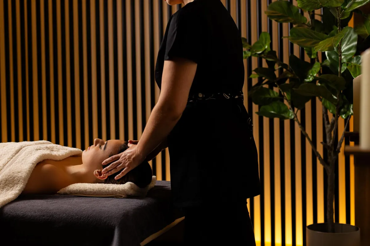 Une personne reçoit un massage crânien allongée sur un lit de massage, tandis qu'une autre personne effectue le massage