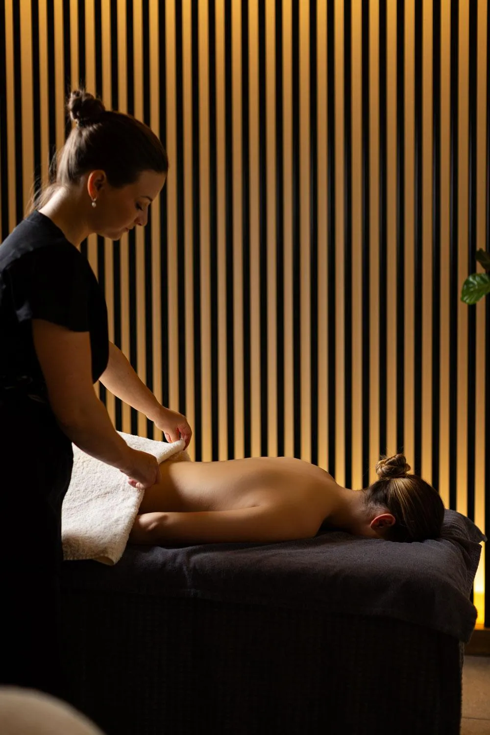 Une personne effectue un massage sur le dos d'une autre personne allongée sur une table dans une pièce aux murs à rayures