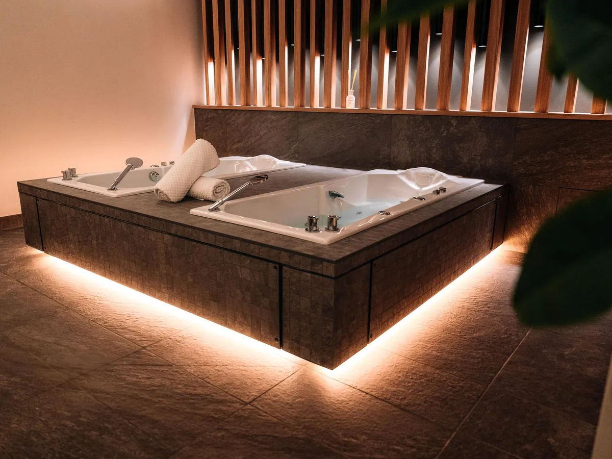 Baignoire à remous encastrée dans un meuble en pierre avec éclairage LED au sol et serviettes blanches posées sur le bord