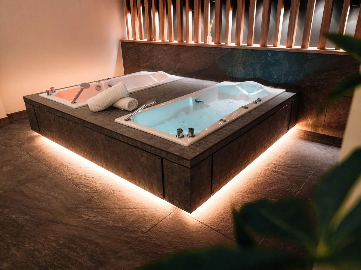 Large built-in whirlpool bathtub in a stone frame with LED floor lighting and towels placed on the edge