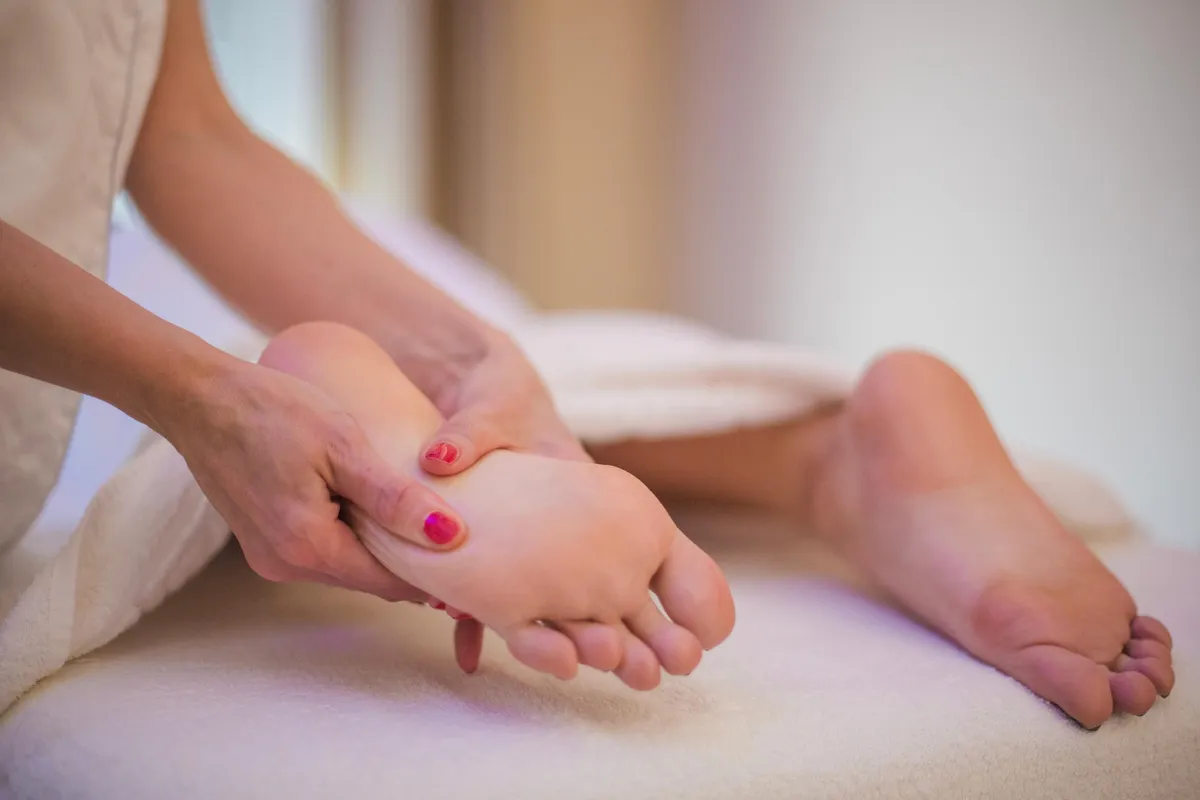 Une personne reçoit un massage des pieds par une autre personne, les pieds ont des ongles vernis de couleurs différentes