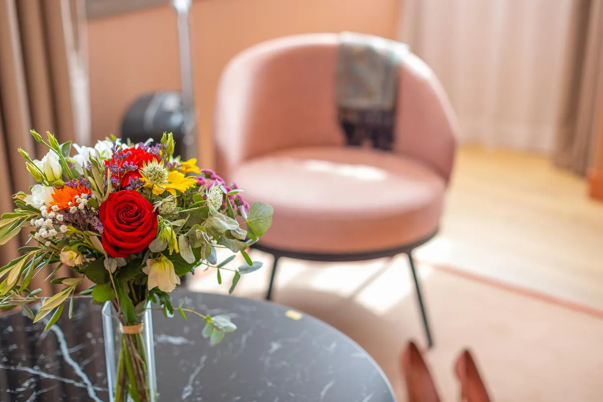 Un bouquet de fleurs colorées dans un vase transparent posé sur une table noire avec des chaises en arrière-plan