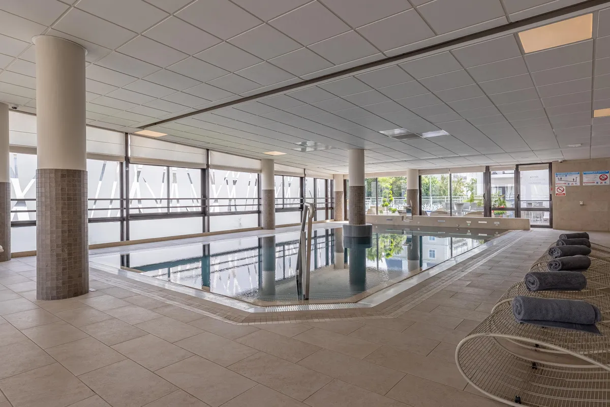 Indoor pool with columns, windows, and towels on lounge chairs