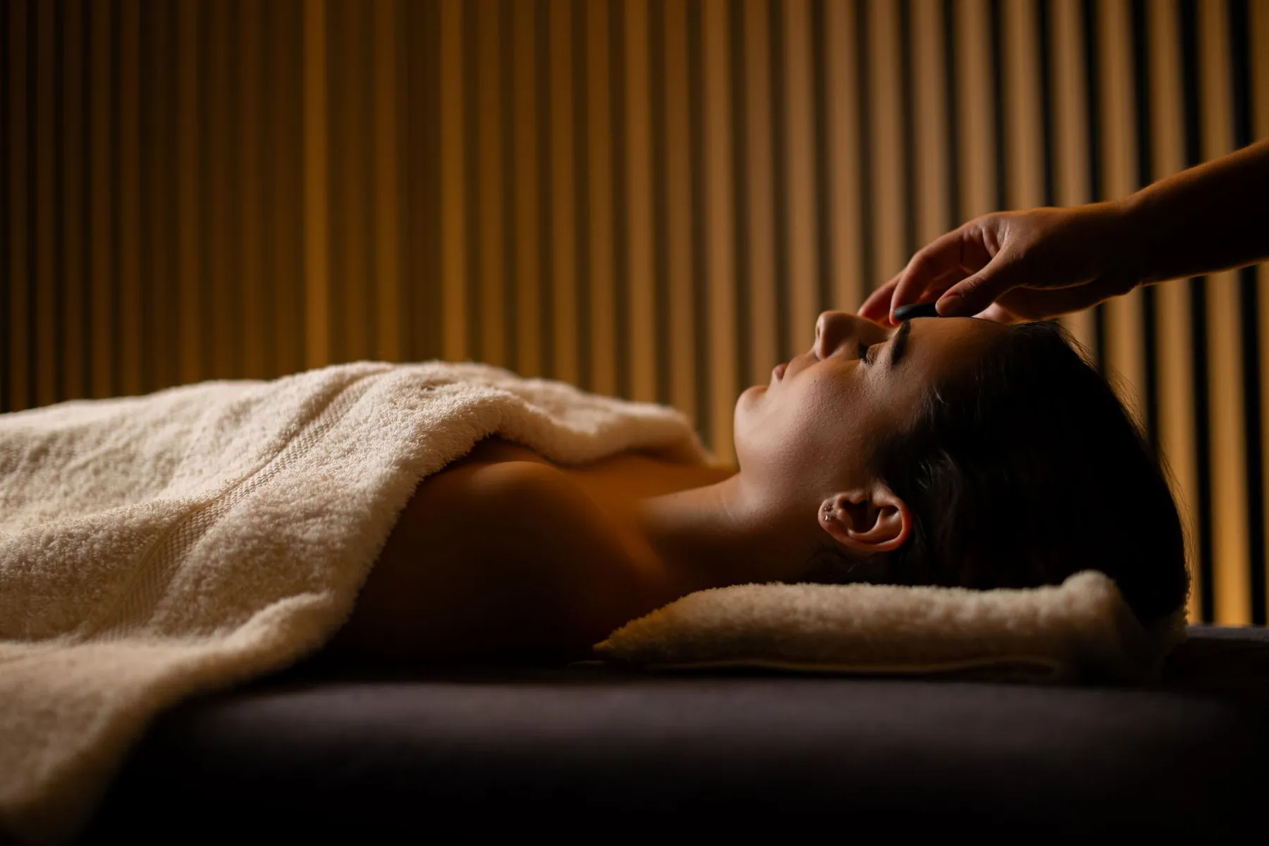 Une personne allongée sur une serviette reçoit un massage facial dans une pièce aux murs striés