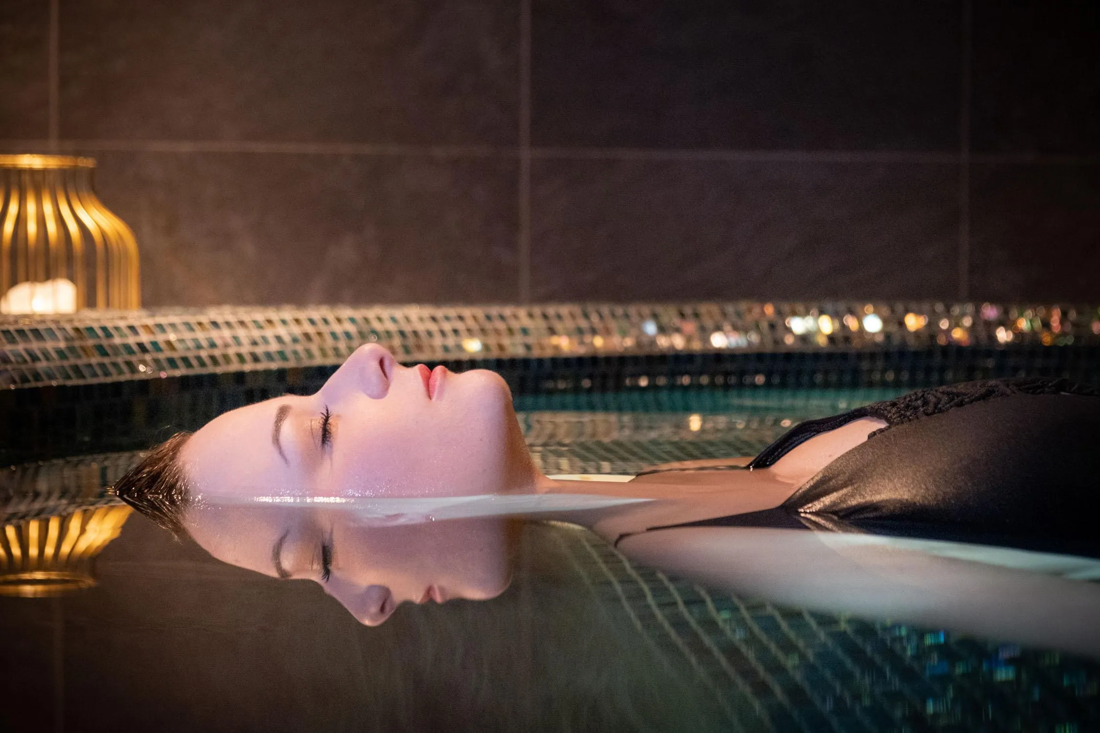Une personne allongée sur le dos dans une piscine avec une vue nocturne de la ville en arrière-plan