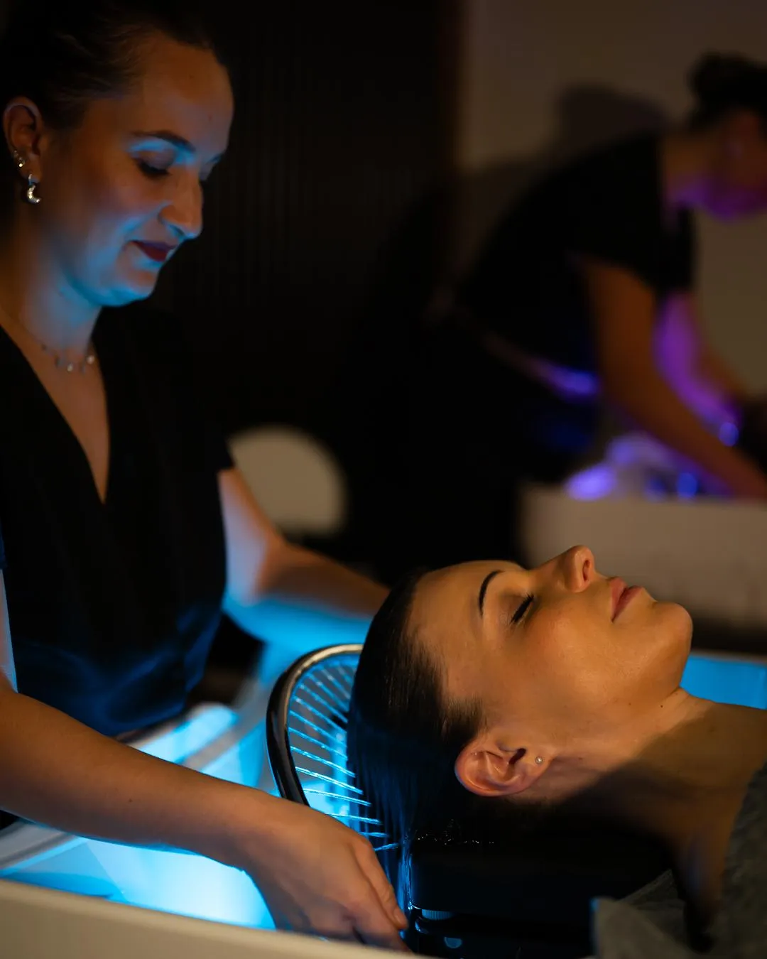 A woman receives a facial treatment in a beauty salon, lying under a blue light.