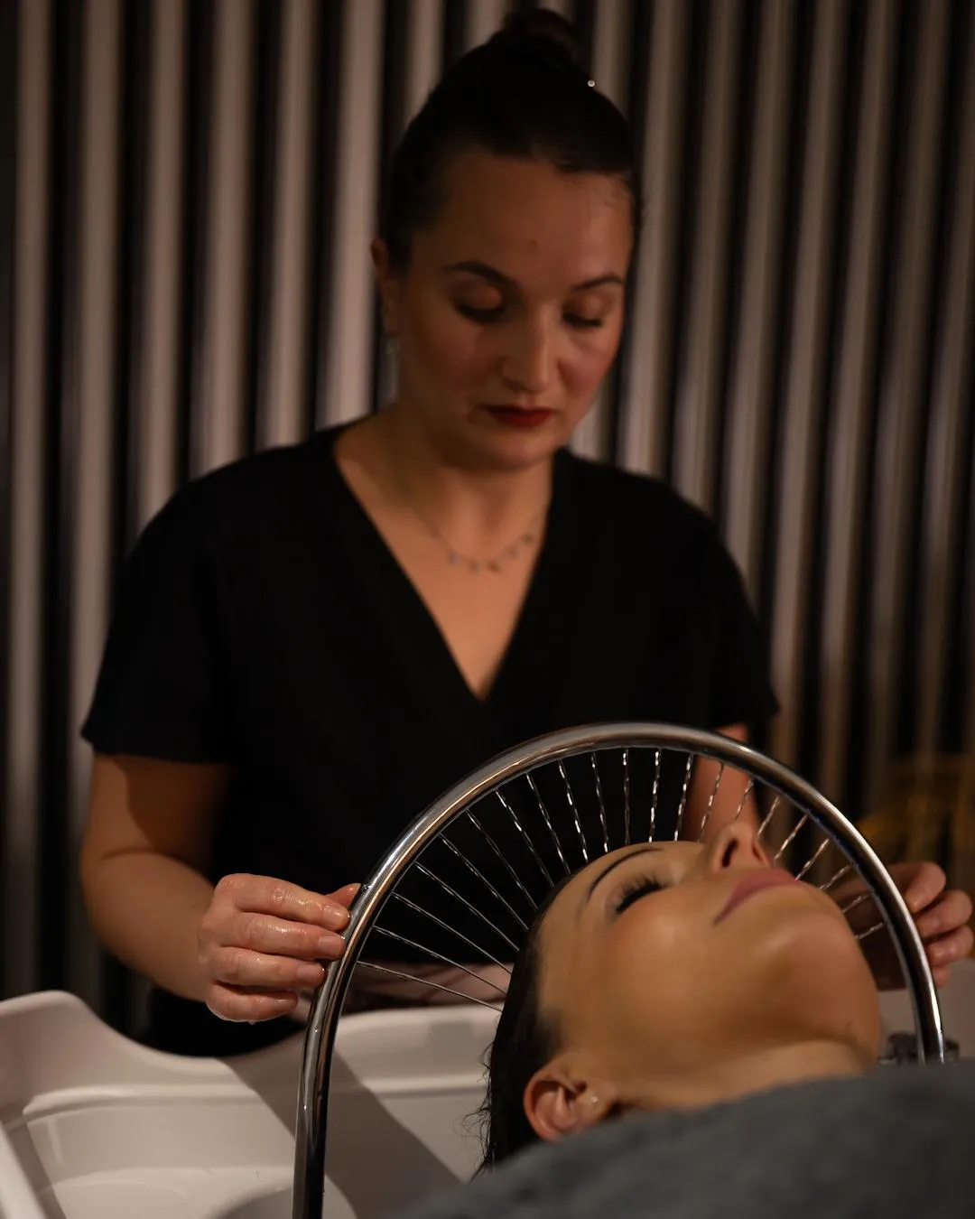 A person is washing the hair of a client lying in a shampoo basin.