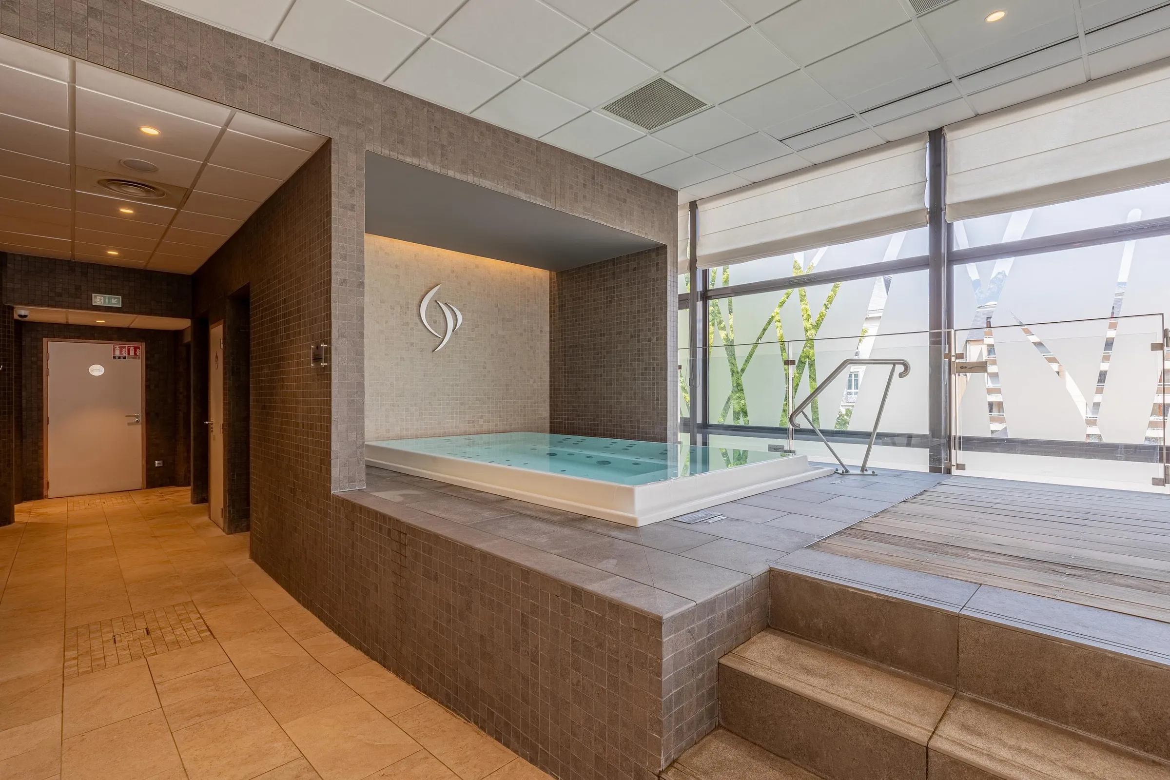 Piscine intérieure avec un mur décoré d'un motif et une grande baie vitrée donnant sur une terrasse extérieure