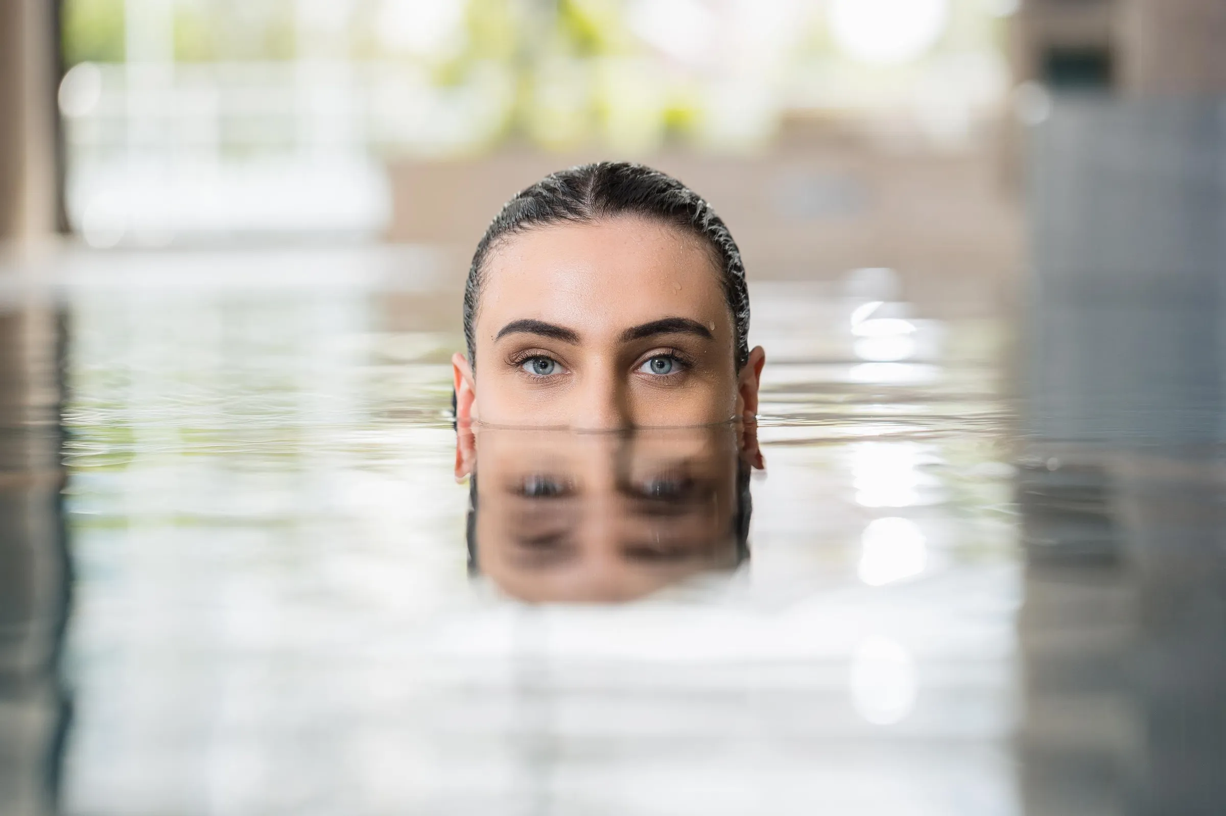 Une personne avec les cheveux attachés émerge de l'eau dans une piscine intérieure