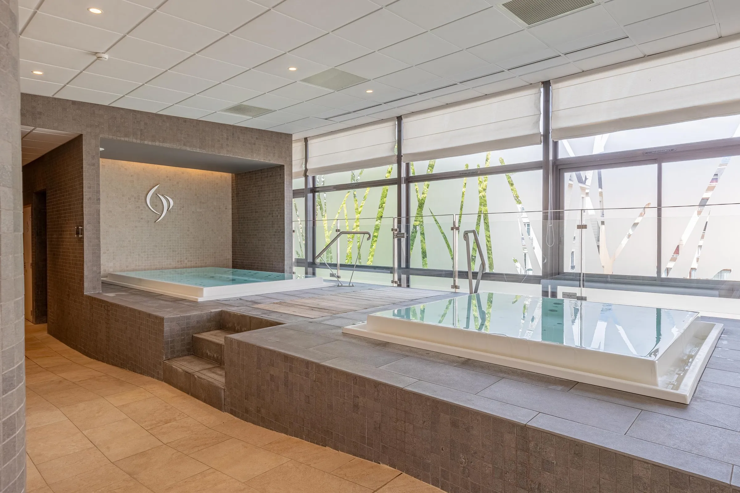 Salle de spa avec deux piscines d'eau chaude et une grande baie vitrée offrant une vue sur une structure extérieure