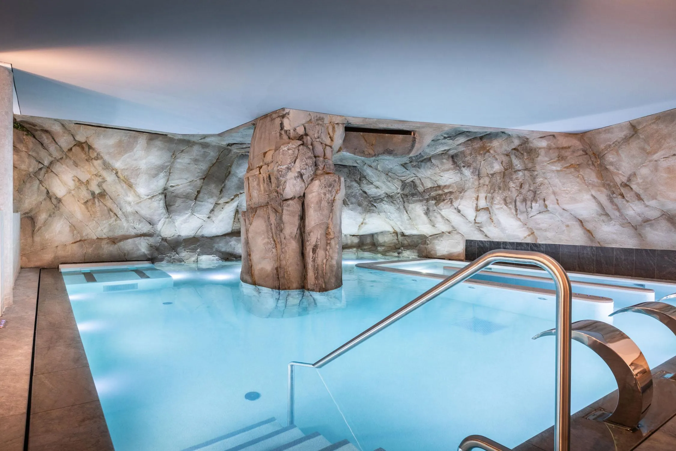 Piscine intérieure avec une grande paroi rocheuse et des marches métalliques pour l'accès