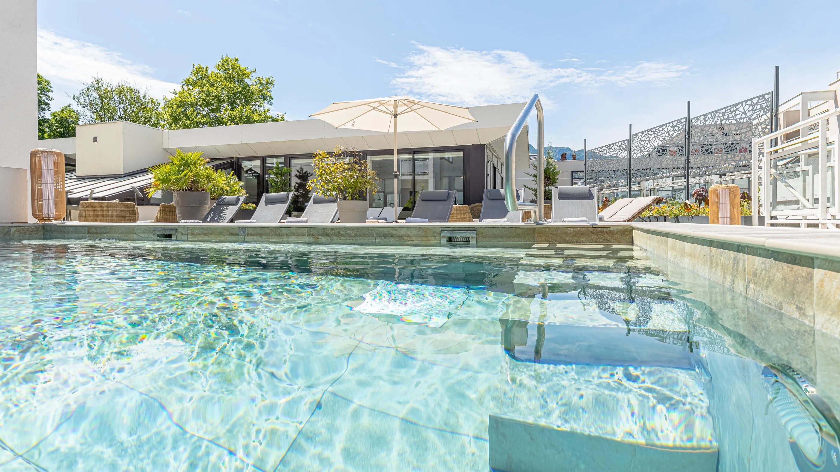 Piscine avec une vue sur un espace de détente extérieur comprenant des transats, des parasols et des plantes en pot