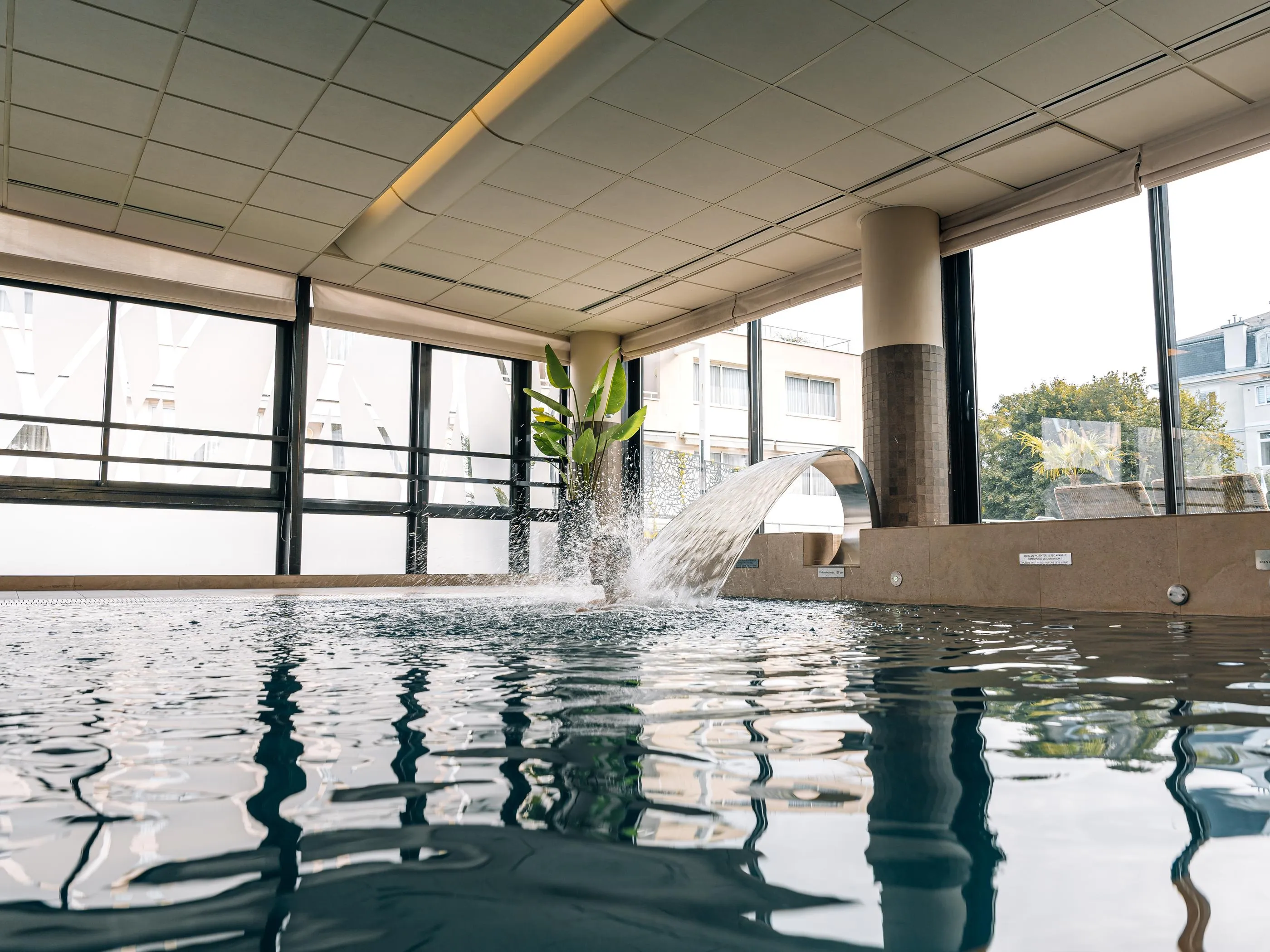 Piscine intérieure avec une fontaine d'eau et des fenêtres donnant sur un bâtiment extérieur